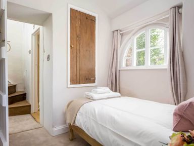 A bedroom with a single bed next to an arched window and wooden door at Stanley Cottage in Chipping Campden