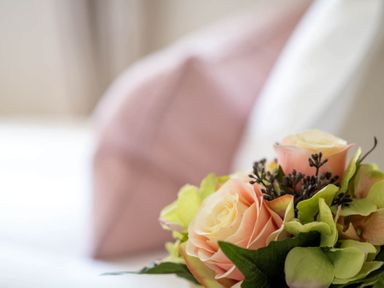 A close up of a bouquet of flowers on a bed with a pink pillow in the background at Stanley Cottage in Chipping Campden