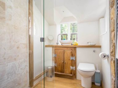 A bathroom with wooden vanity cabinet a white vessel sink a toilet and a glass shower at Stanley Cottage in Chipping Campden