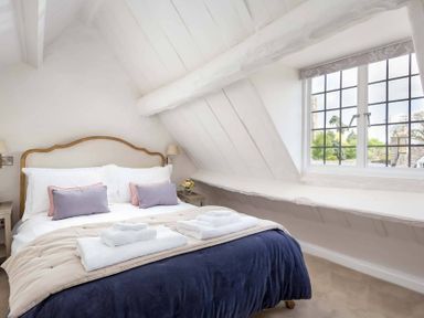 A bedroom with a bed made with white and beige bedding and towels on top at Stanley Cottage in Chipping Campden