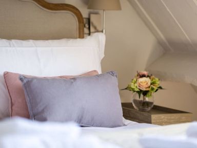 A bed with pillows and a bedside table with a vase of flowers at Stanley Cottage in Chipping Campden