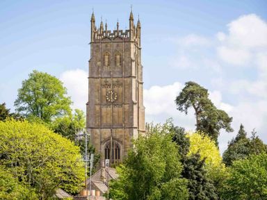 A stone clock tower surrounded by trees and rooftops at Stanley Cottage in Chipping Campden