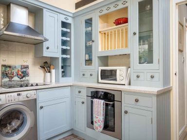 A kitchen with light blue cabinets a washing machine a stove a microwave and utensils at Lanes Cottage in Chipping Campden