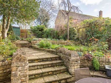 A garden with stone steps leading to a raised area with plants and trees at Lanes Cottage in Chipping Campden