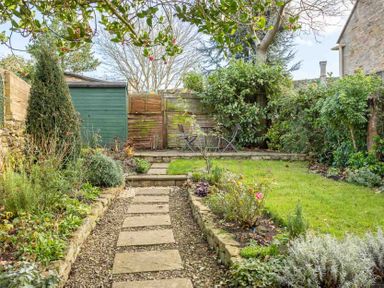 A garden with a stone path leading to a small patio with a table and two chairs at Lanes Cottage in Chipping Campden