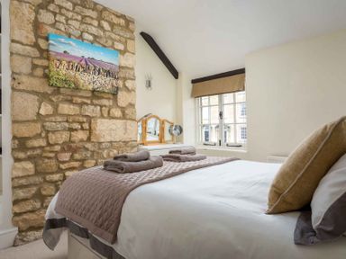 A bedroom with a stone feature wall a bed with folded towels and a window with a dressing table at Lanes Cottage in Chipping Campden