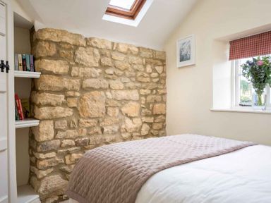 A bedroom with a stone wall a skylight a window with flowers and a bed at Lanes Cottage in Chipping Campden