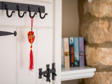 A wall hook with a red decorative hanging and a small white shelf with books at Lanes Cottage in Chipping Campden