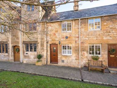 A stone cottage exterior with wooden doors windows a bench and plants at Lanes Cottage in Chipping Campden