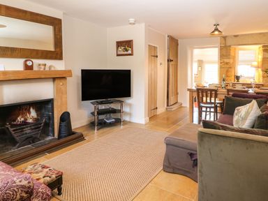 A living room with a fireplace a TV a dining table and sofas at Green Pump Cottage in Blockley