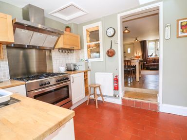 A kitchen with a gas stove oven toaster and a wooden stool leading to a dining area at Green Pump Cottage in Blockley