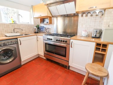 A kitchen with a stove a washing machine a toaster and a stool at Green Pump Cottage in Blockley