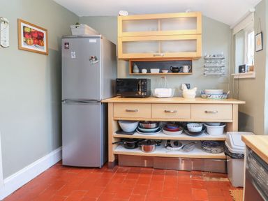 A kitchen area with a refrigerator wooden cupboard microwave and shelves with dishes at Green Pump Cottage in Blockley
