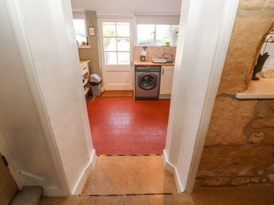 A view into a kitchen with a washing machine a sink a door and tiled floor at Green Pump Cottage in Blockley