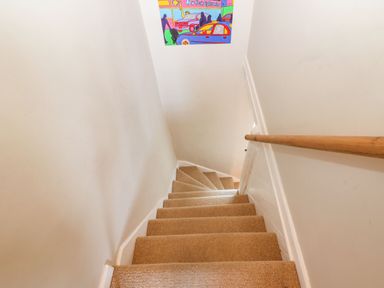 A carpeted staircase with a wooden handrail and a colorful poster on the wall at Green Pump Cottage in Blockley