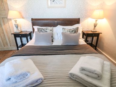 A bedroom with a double bed two bedside tables with lamps and folded towels at Green Pump Cottage in Blockley
