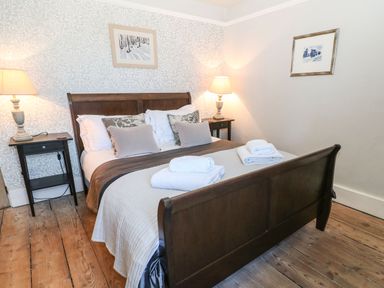 A bedroom with a wooden bed frame bedside tables with lamps and folded towels on the bed at Green Pump Cottage in Blockley