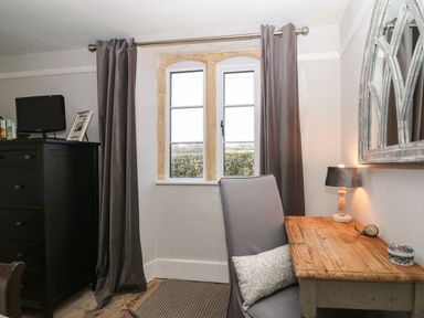 A room with a wooden desk and chair by a window with dark curtains and a black chest of drawers with a small TV on top at Green Pump Cottage in Blockley