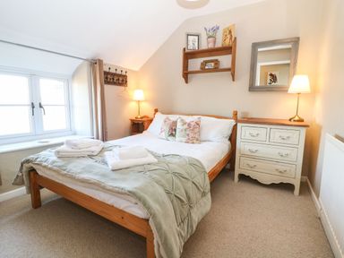 A bedroom with a wooden bed covered with a light green comforter and towels on top at Green Pump Cottage in Blockley