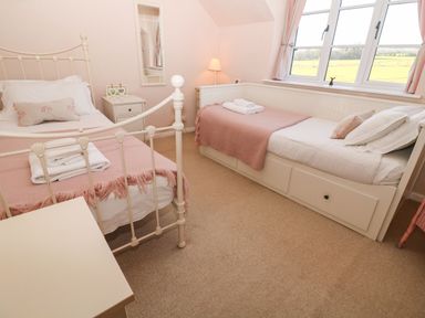 A bedroom with two single beds a lamp and a window with curtains at Green Pump Cottage in Blockley