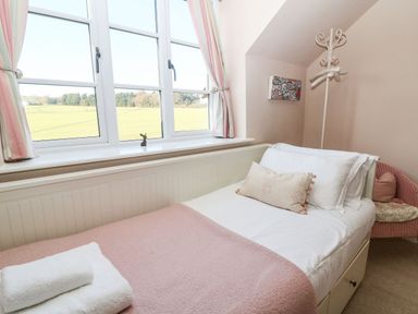 A bedroom with a single bed covered with white and pink bedding near a window with pink striped curtains at Green Pump Cottage in Blockley