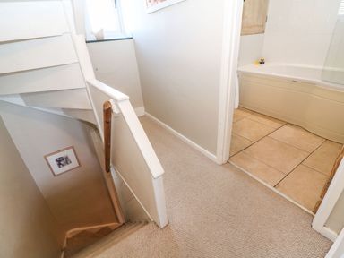 A stairway with beige carpet leading down with a handrail and a hallway leading to a bathroom with a bathtub at Green Pump Cottage in Blockley