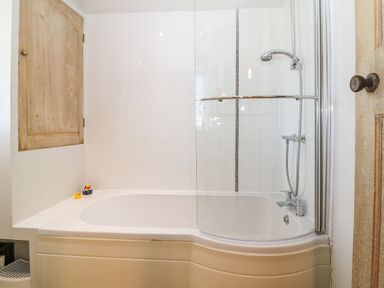 A bathroom with a bathtub shower combination wooden cabinet and two rubber ducks at Green Pump Cottage in Blockley