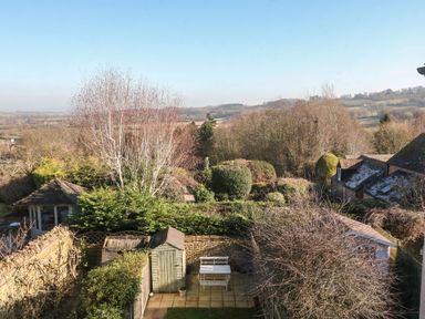 A backyard with garden sheds white bench trees and hills in the background at Green Pump Cottage in Blockley