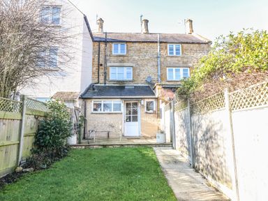 A backyard with grass lawn and a concrete path leading to a stone cottage with an extension at Green Pump Cottage in Blockley