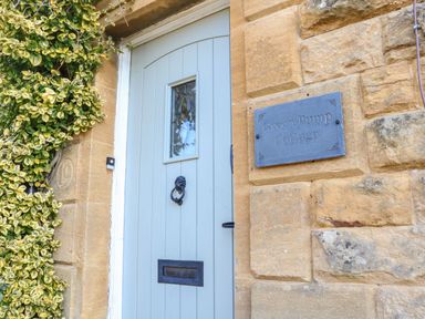 A pale blue door with a mail slot and lion head knocker next to a sign that reads Green Pump Cottage on a stone wall at Green Pump Cottage in Blockley