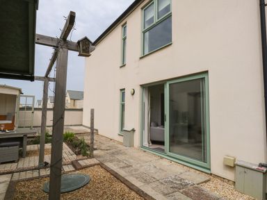 A backyard patio with sliding glass door wooden pergola and garden beds at Pebbles Reach in Fortuneswell