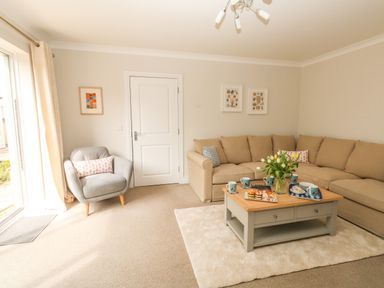 A living room with a beige sectional sofa a grey armchair a wooden coffee table with snacks and flowers at Pebbles Reach in Fortuneswell