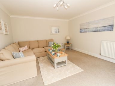 A living room with beige sectional sofa a wooden coffee table with cups flowers and snacks and paintings on the wall at Pebbles Reach in Fortuneswell
