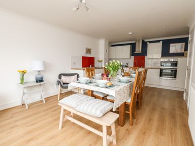 A dining area with a table set with dishes and flowers and a kitchen with white cabinets and red panels at Pebbles Reach in Fortuneswell
