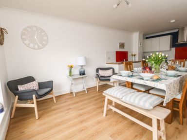 A dining area with a wooden table set with dishes and flowers two armchairs a bench with cushions and a clock on the wall at Pebbles Reach in Fortuneswell