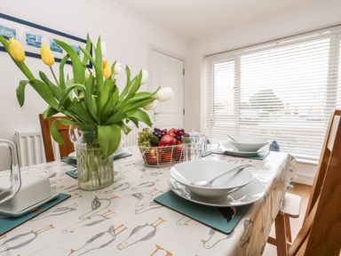 A dining table set with bowls, glasses, a fruit basket, and a vase of yellow and white tulips at Pebbles Reach in Fortuneswell