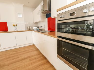 A kitchen with white cabinets wooden countertops a double oven and a glass cooktop at Pebbles Reach in Fortuneswell