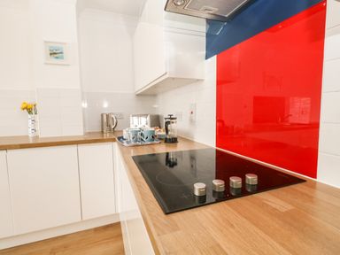 A kitchen with a stovetop on a wooden counter a red backsplash mugs and a kettle on the counter at Pebbles Reach in Fortuneswell