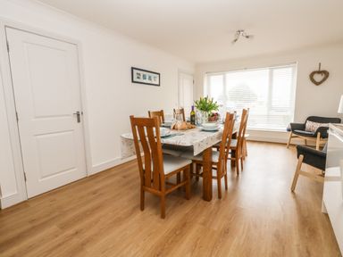 A dining room with a wooden table and chairs set for a meal near a large window at Pebbles Reach in Fortuneswell