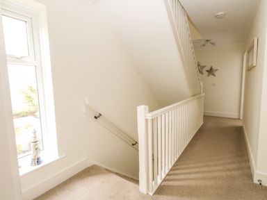 A hallway with carpeted floor stairs and a window with a small lighthouse decoration at Pebbles Reach in Fortuneswell