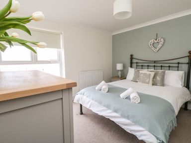 A bedroom with a bed table lamp and a dresser with flowers at Pebbles Reach in Fortuneswell