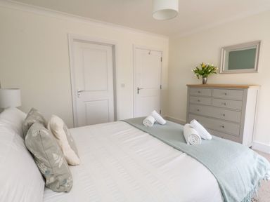 A bedroom with a bed with pillows and rolled towels a gray dresser with a vase of flowers and a mirror on the wall at Pebbles Reach in Fortuneswell