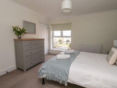 A bedroom with a bed, dresser, mirror, and flowers on the dresser at Pebbles Reach in Fortuneswell