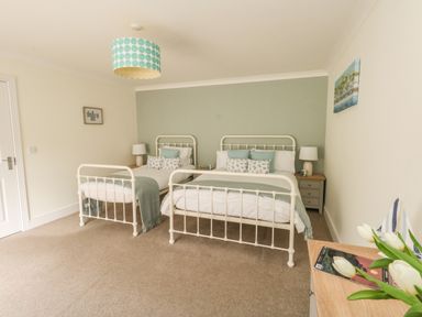 A bedroom with two metal beds side by side bedside tables with lamps and a wooden dresser with flowers at Pebbles Reach in Fortuneswell