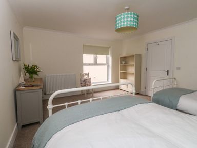 A bedroom with two single beds a chair a bookshelf and a cabinet with flowers at Pebbles Reach in Fortuneswell
