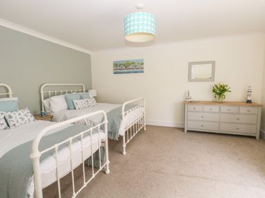 A bedroom with two metal frame beds a gray dresser with flowers and decorations on top at Pebbles Reach in Fortuneswell