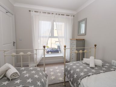 A bedroom with two single beds with star patterned blankets a chest of drawers and a window with sheer curtains at Pebbles Reach in Fortuneswell