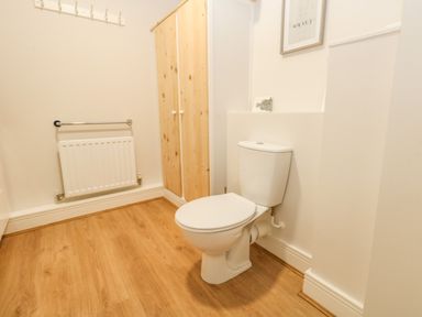 A bathroom with a toilet wooden floor wooden cabinet white radiator and towel rail at Pebbles Reach in Fortuneswell