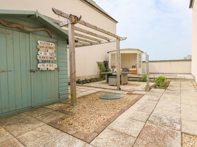 An outdoor patio area with a green shed and wooden pergola near a small seating area at Pebbles Reach in Fortuneswell