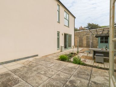An outdoor patio area with tiled flooring a small garden a wooden pergola table and chairs and a light green shed at Pebbles Reach in Fortuneswell